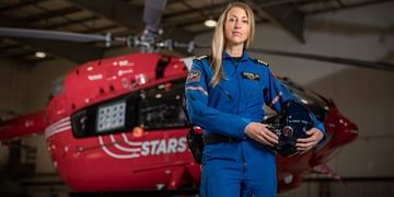 Portrait of STARS Calgary Aviation Base Manager and pilot as she stands with her helmet under one arm, posed in front of a STARS H145 air ambulance helicopter in a STARS hangar.