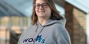 Person wearing glasses and a gray "Wolves" hoodie, smiling at the camera with a blurred building background.