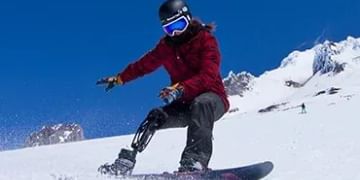 Skier in red jacket descending snowy slope against clear blue sky with snow-covered mountains in the background