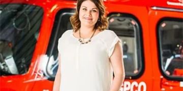 Person in white shirt standing in front of red emergency vehicle with windows and equipment visible in background