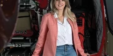 Woman in pink cardigan and jeans standing in front of red vehicle with open door, smiling at camera