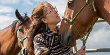 Person in striped clothing holding the halter of a brown horse against a blue sky with clouds