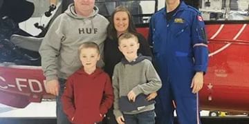 Family of five posing in front of a red and purple aircraft inside a hangar, with an adult in blue flight suit standing beside them.