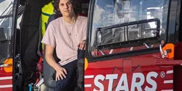 Person in pink shirt sitting in red emergency vehicle with "STARS" written on side, wearing safety gear and looking at camera