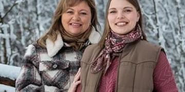 Two people smiling at the camera in winter clothing against a snowy forest background with frost-covered trees