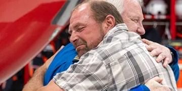 Two men embracing in a warm hug at what appears to be a public event with red signage in the background