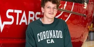 Young person wearing a dark green "Coronado CA" sweatshirt standing in front of a red vehicle with partial "STARCO" text visible