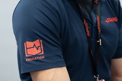 Person wearing navy polo shirt with red "EDUCATION" logo featuring a heartbeat symbol and red "STARS" text on lanyard