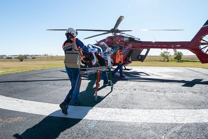 Medical helicopter with crew members on landing pad in rural area with flat grassland and clear sky