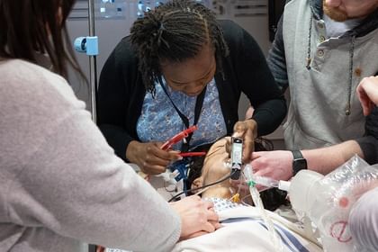 Group of people gathered around a table working on an electronics or engineering project with tools and components during what appears to be a hands-on workshop or educational demonstration.
