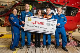 STARS ally Cindy Letourneau poses alongside STARS operations crew members during a cheque presentation at the STARS base in Calgary. The cheque recognizes the total donated amount of $253,780 that Cindy has raised in honour of her son Chris who was flown by STARS in 2013, but passed from his injuries shortly after.