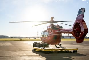 A STARS air ambulance helicopter is towed outside of the Calgary hangar before taking off. The sun rises in the background, indicating an early morning mission.
