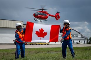 STARS air medical crew hold a Canada flag while a STARS air ambulance helicopter hovers in the background.