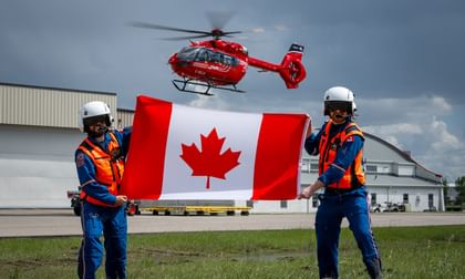 STARS air medical crew hold a Canada flag while a STARS air ambulance helicopter hovers in the background.