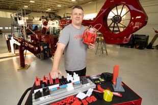 STARS aircraft maintenance engineer Ryan Gillis stands alongside some of the 3D printed work aids the engineering team has developed to help streamline their work. A STARS air ambulance helicopter sits in the background, undergoing maintenance at the STARS Edmonton hangar.