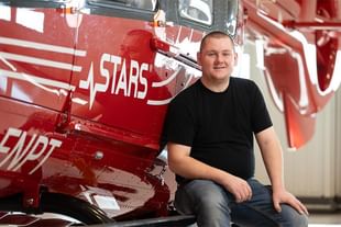 Person in black shirt sitting in front of red fire truck with white lettering and stripes