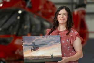 Artist, writer, and STARS Very Important Patient Shelly Campbell holds her artwork titled Golden Hour in front of a STARS air ambulance helicopter during a visit to her closest STARS base. The artwork was commissioned by STARS for inclusion in the 2027 STARS Calendar.
