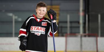 STARS Very Important Patient Beckham Koscielny leans on a hockey stick at his local rink while wearing a STARS Winnipeg Base hockey jersey.