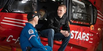 STARS Very Important Patient Broc Higginson sits in the open side door of a STARS air ambulance helicopter while talking with a member of STARS operations staff.