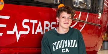 STARS Very Important Patient Hudson Blough poses in front of the STARS logo on a STARS air ambulance helicopter during a visit to a STARS base.