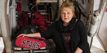 STARS Very Important Patient Peggy Benko sits in the open back door of a STARS air ambulance helicopter. With the doors open, the interior of the medical cabin is visible.