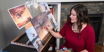 Artist, writer, and STARS Very Important Patient Shelly Campbell paints at an easel in her home, working on her artwork she's called Golden Hour, a commissioned piece of art that was created for the 2027 STARS Calendar.