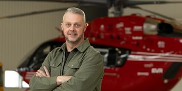 STARS Very Important Patient Trevor Mills poses with arms crossed in front of a STARS air ambulance helicopter during a visit to his closest STARS base.