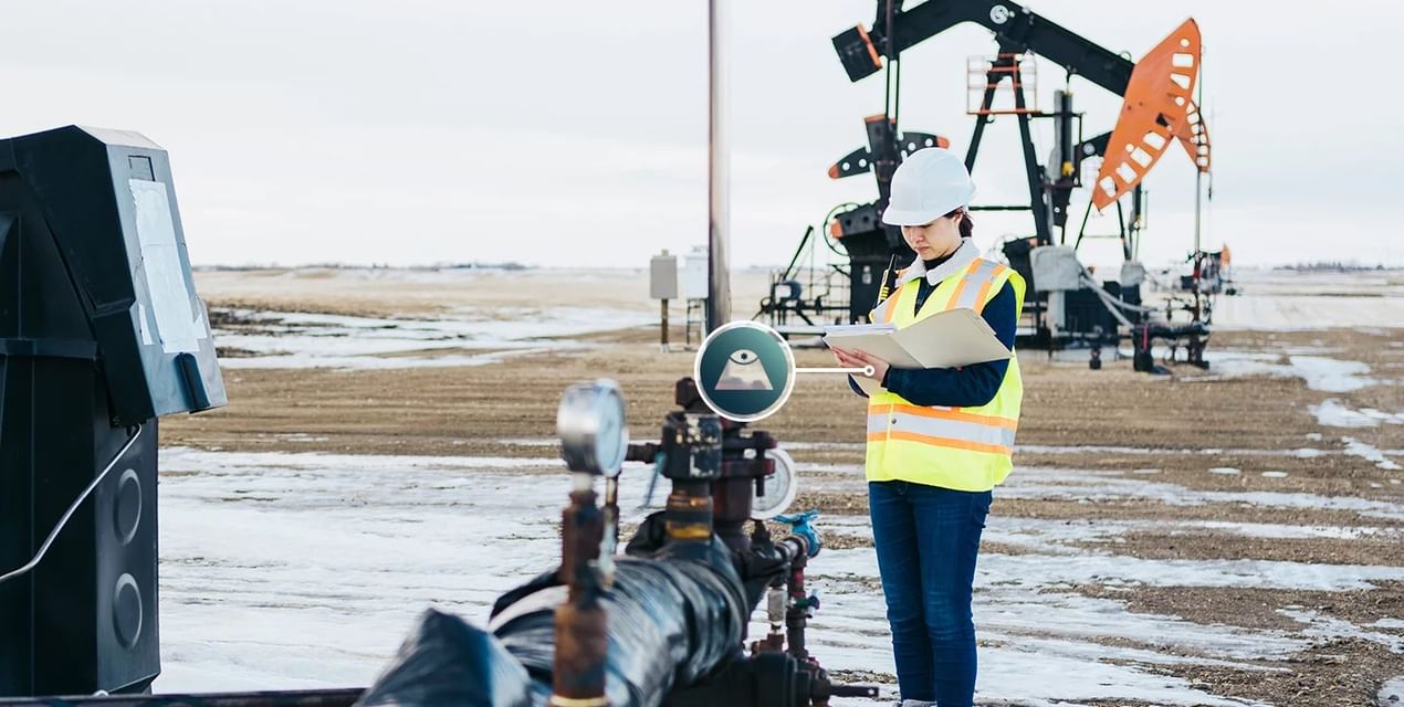 A stock image of a woman in a safety vest and hard hat at an oil and gas wellsite, making notes on a clipboard. A Vigilant work along monitoring icon is superimposed over a part of the image.