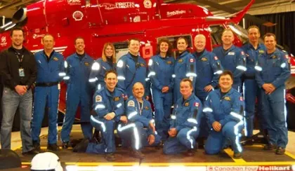 A group of 15 people in STARS flight suits pose for a photo next to a red helicopter.
