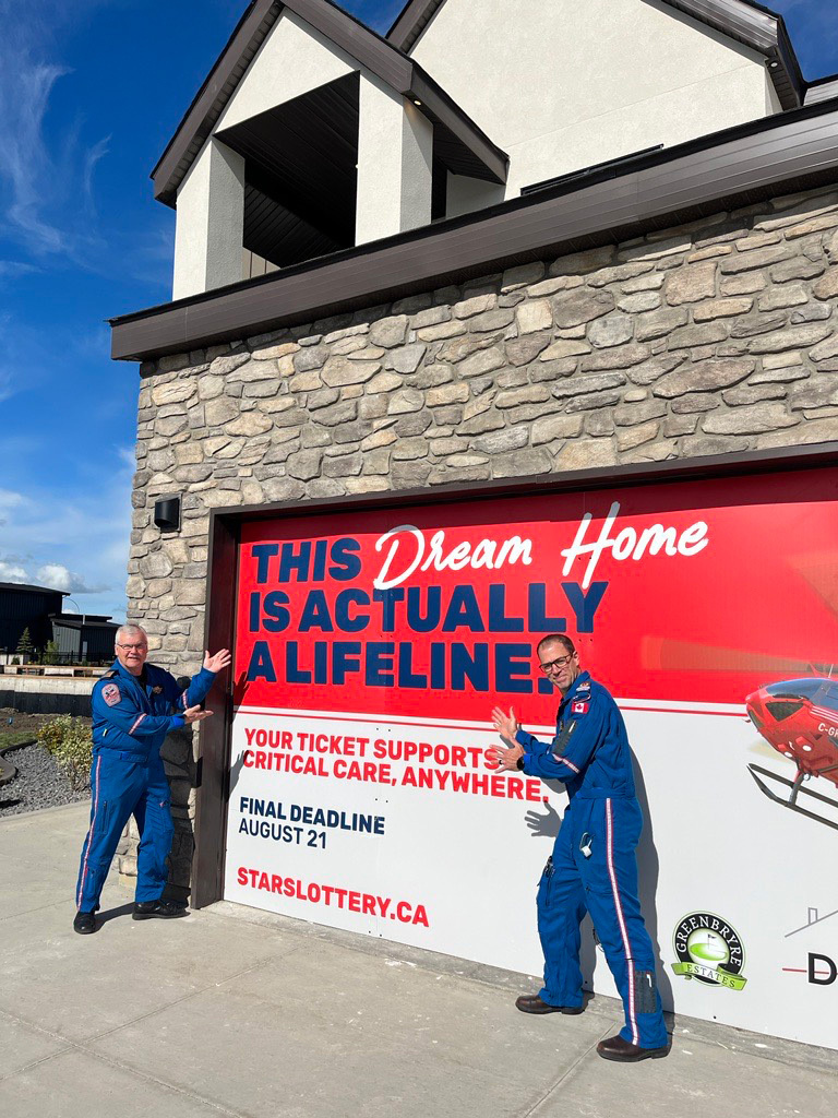 STARS operations staff pose outside the STARS LOTTERY Saskatchewan dream home in Saskatoon, highlighting the temporary vinyl signage on the garage door promoting the lottery.