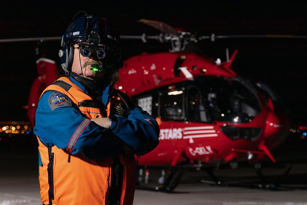 STARS Pilot, Captain Phil Haworth, poses in front of a STARS H145 air ambulance at night while wearing his flight helmet with night vision goggles equipped.