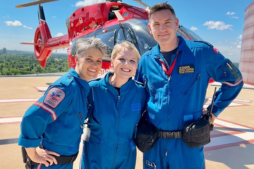 A photo of Kaitlyn Julas standing between STARS flight nurse Krista Hartmass and STARS flight paramedic Michael Christian, posed in front of a STARS H145 air ambulance.