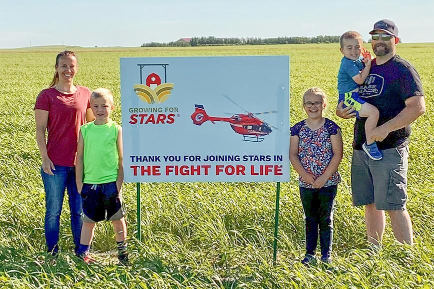 STARS Very Important Patient and ally Ryley Richards stands with his family on one of the crop fields with a Growing for STARS sign, part of a program that donates crop proceeds to STARS.