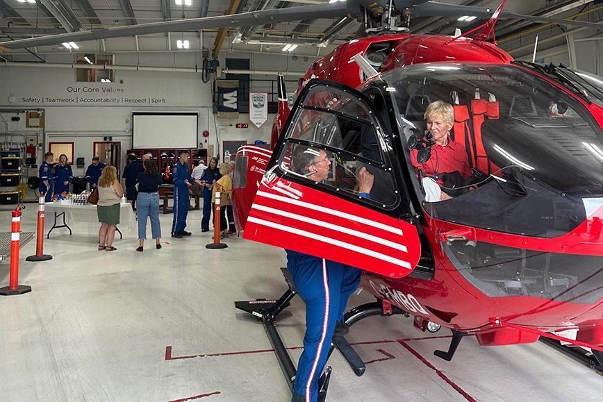 Attendees tour the STARS Winnipeg hangar during an open house at the STARS Winnipeg Base in celebration of STARS' 40th Anniversary. One attendee sits in the cockpit of a STARS H145 air ambulance helicopter, while a STARS pilot explains a detail. Other attendees are in the background talking to STARS operations staff.