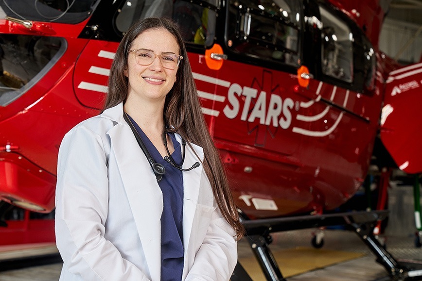 STARS Transport Physician Dr. Darla Palmer poses in her lab coat and stethoscope in front of a STARS H145 helicopter.