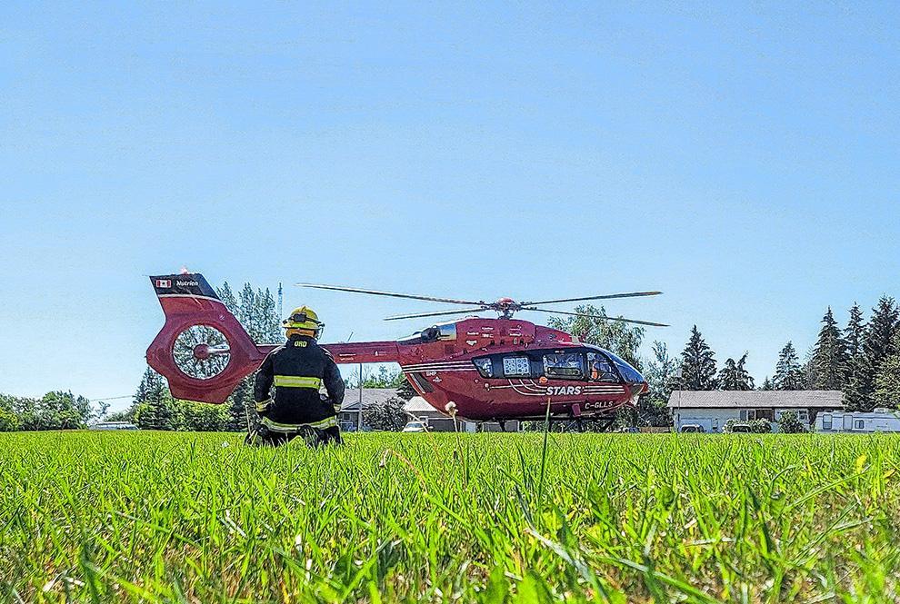 A STARS H145 air ambulance in a field in Saskatchewan with a firefighter who has helped land the helicopter is in the foreground.