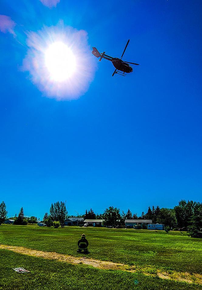 The STARS air ambulance shortly after taking off from the scene of Draidyn's incident. A firefighter kneels on the ground having assisted with the landing zone.